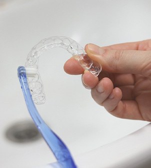 Patient using toothbrush to clean aligners in sink