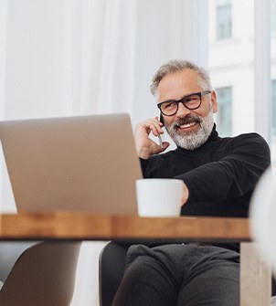 Man with glasses smiling while working on laptop