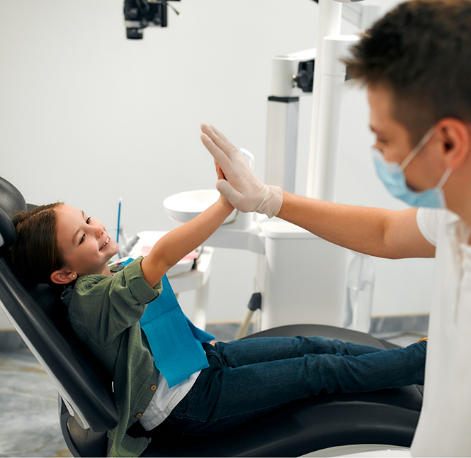 Young girl in the dental chair giving a high five to her dentist