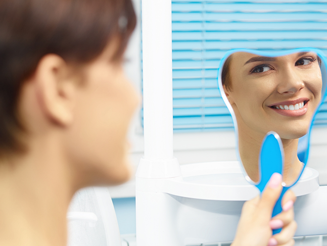 Dental patient looking at her smile in a tooth-shaped mirror