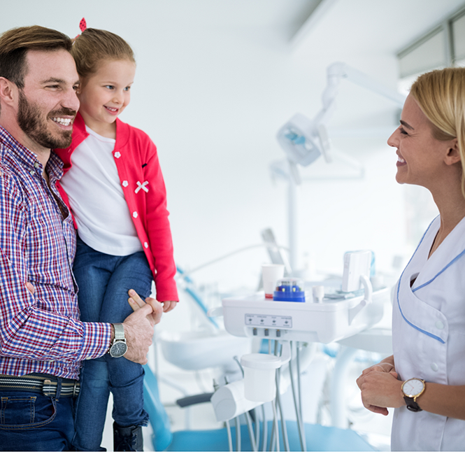 Father and his young daughter talking to a dentist during a checkup