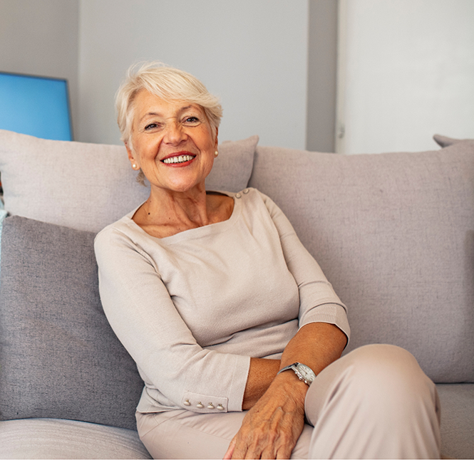 Senior woman sitting on a couch and smiling with dentures in San Antonio