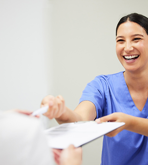 Smiling dental team member handing a clipboard to a patient