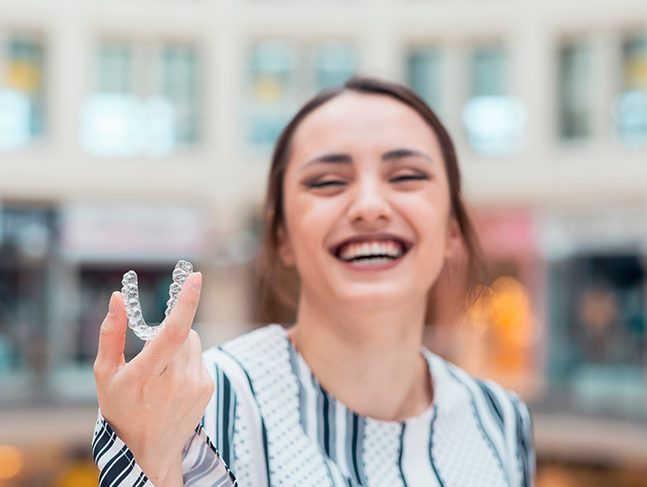 Smiling brunette woman holding Invisalign