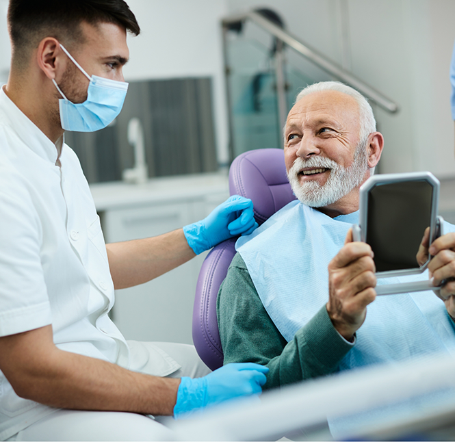 Senior dental patient admiring his smile in a mirror after replacing missing teeth
