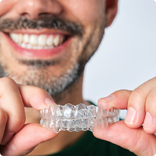 Smiling man holding two Invisalign clear aligners