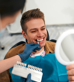 Man looking at his smile in a mirror while a dentist holds veneers to his teeth