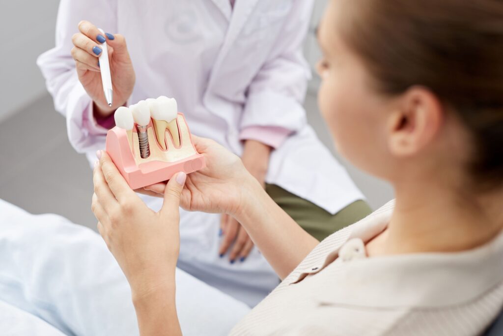 Woman holding sample dental implant as dentist points with pen